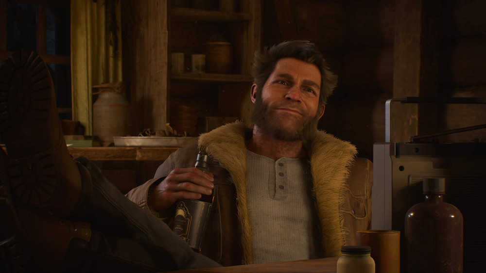 Logan con una botella de whisky en la mano, sonriendo, sentado con los pies sobre la mesa